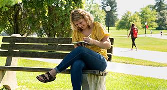 An image of student writing on a bench on campus